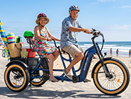 Two riders pedaling together at different speeds on a versatile tandem electric tricycle with independent drivetrains.